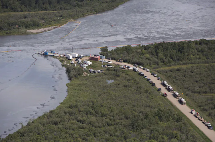 People and vehicles stand near an oily river.