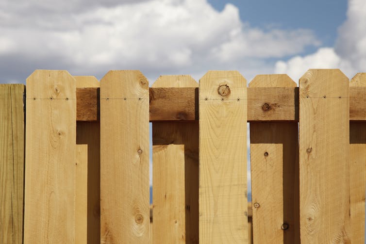 A light-colored wood fence set against a cloudy sky.