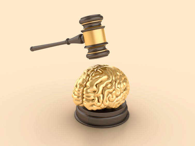 A tiny golden brain, about to hit by a wooden gavel with a gold band on it.