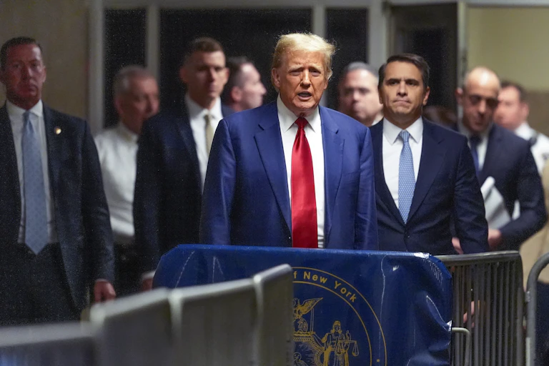 A white man wearing a dark business suit is surrounded by other men wearing dark suits.