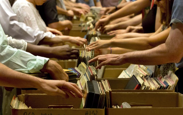 Many people's hands and arms are seen browsing through boxes of records at the New York Public Library