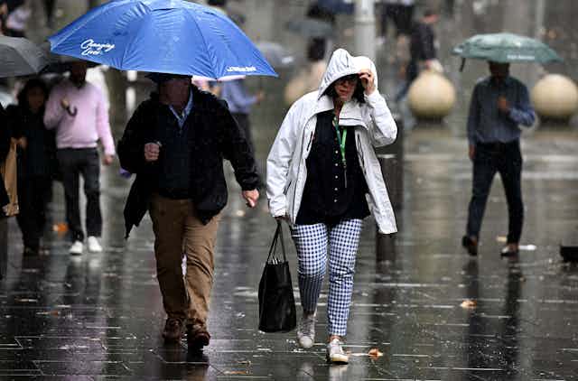 Two people walk through rain in Sydney wearing raincoats and holding umbrellas.