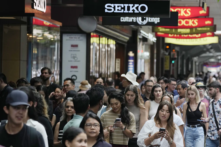A crowd of shoppers walk passed illuminated shop signs in the street.
