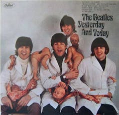 The four Beatles are in white lab coats and surrounded by decapitated dolls and raw meat
