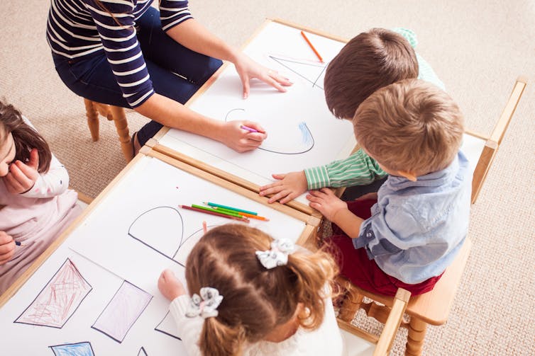 Children seen at a table colouring around letters.