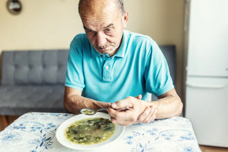 Person holding up arm with opposite hand to lift a spoonful of soup