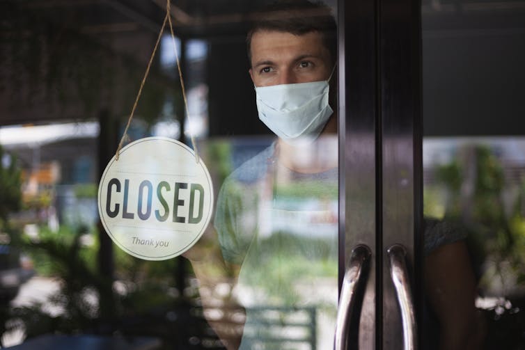 A worker with a face mask stands inside a cafe with a 'closed' sign on the glass window.