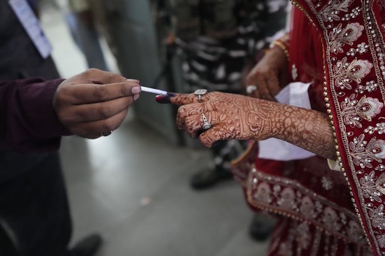 A man applies ink on the finger of a woman's hand, that is decked with an intricate pattern of henna.