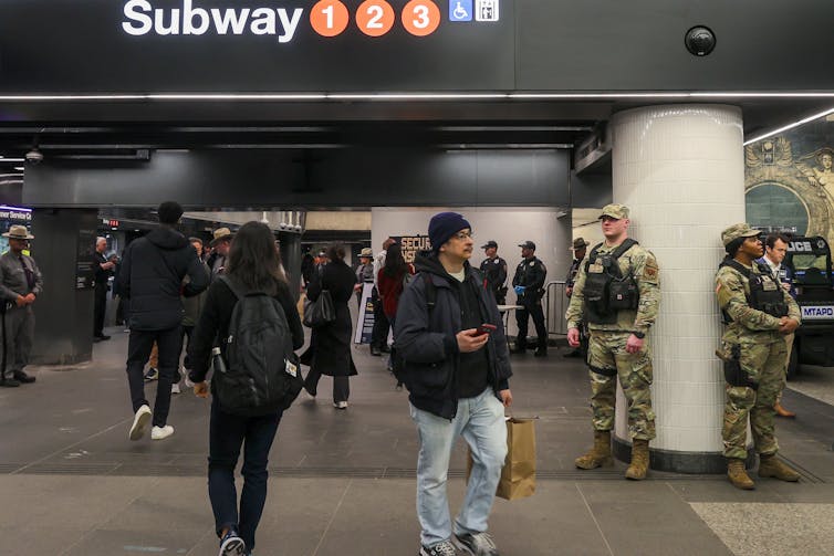 National guard troops look out over small crowd of commuters at an NYC subway station