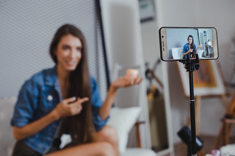 A young woman filming herself sitting and talking with a cellphone