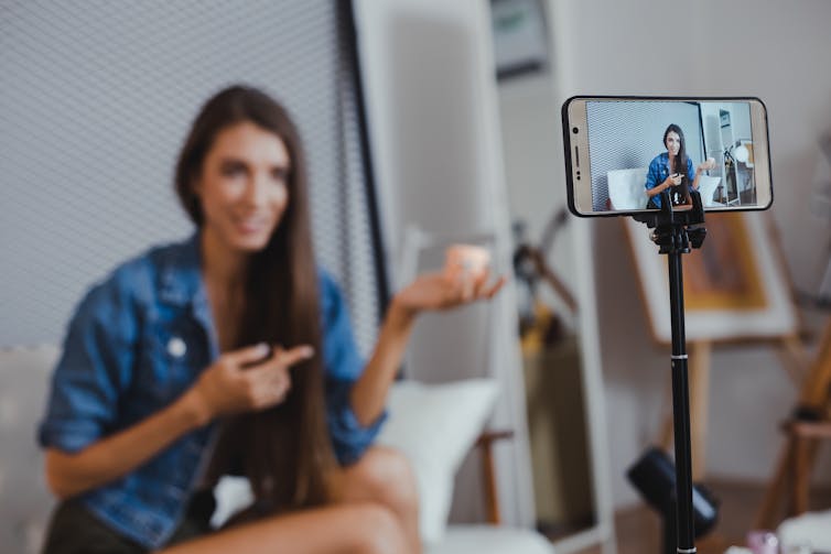 Young woman filming herself sitting and talking on mobile phone