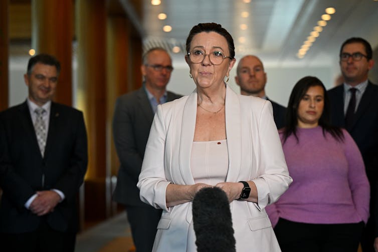 A woman in a blazer stands in front of a microphone and gives a speech
