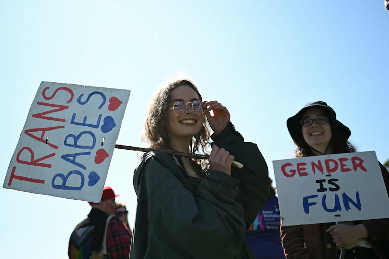 A protester holds a sign in support of transgender rights and another holds a sign reading 'gender is fun'.