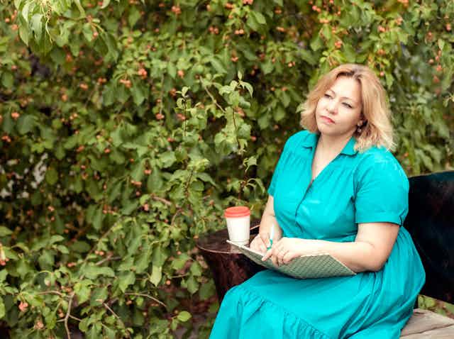 Woman looks unhappy sitting on park bench with notepad