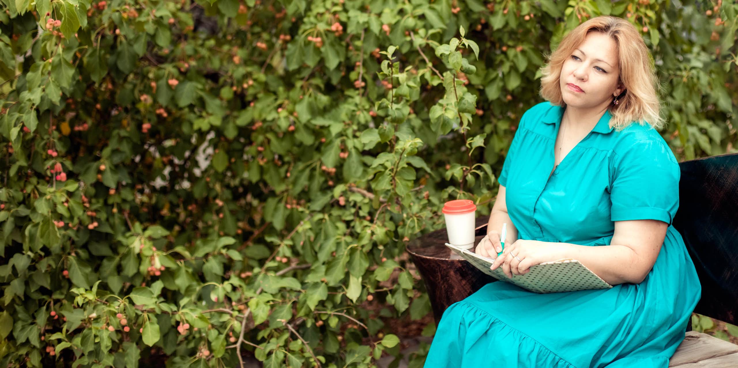 Woman looks unhappy sitting on park bench with notepad