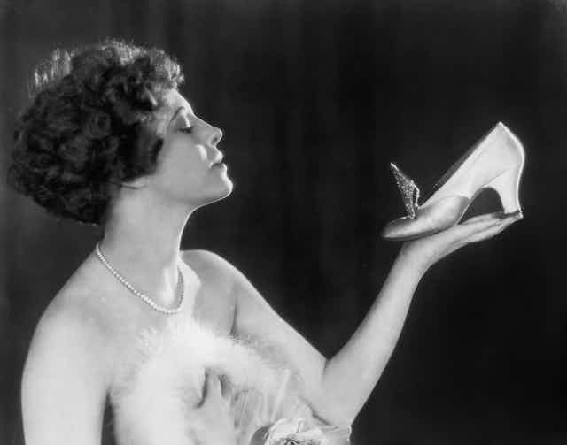 A 1940s woman holds a heeled shoe in one hand while looking at it