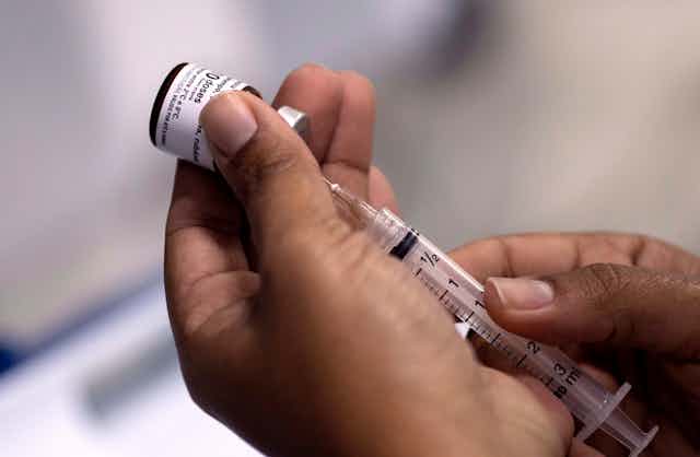 Hands filling a syringe from a vial of vaccine