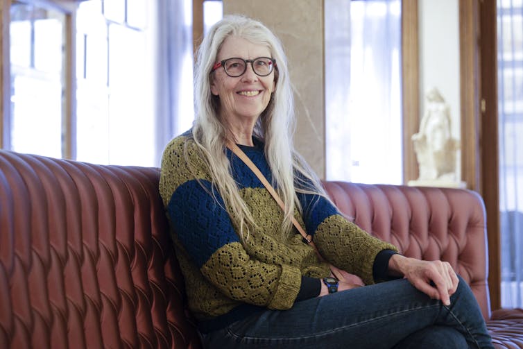 A woman with long hair (Jane Smiley) sitting on a red couch.