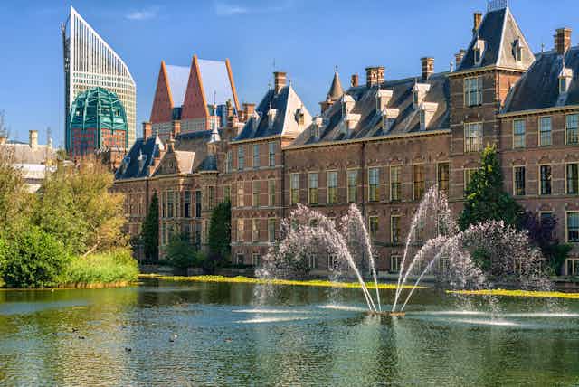 Binnenhof Palace big grand building in Netherlands with water fountain and lake in foreground, blue sky