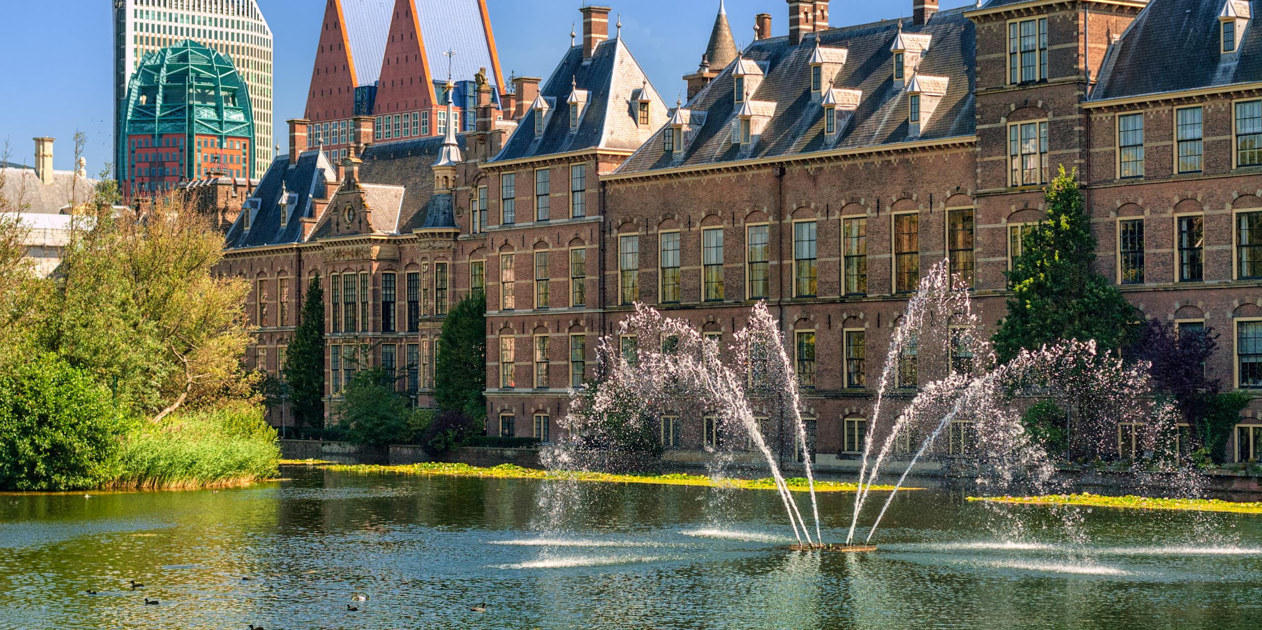 Binnenhof Palace big grand building in Netherlands with water fountain and lake in foreground, blue sky