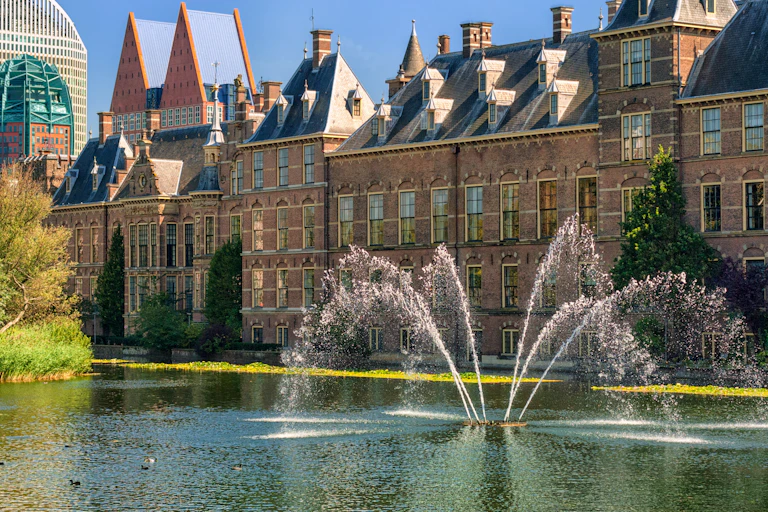 Binnenhof Palace big grand building in Netherlands with water fountain and lake in foreground, blue sky