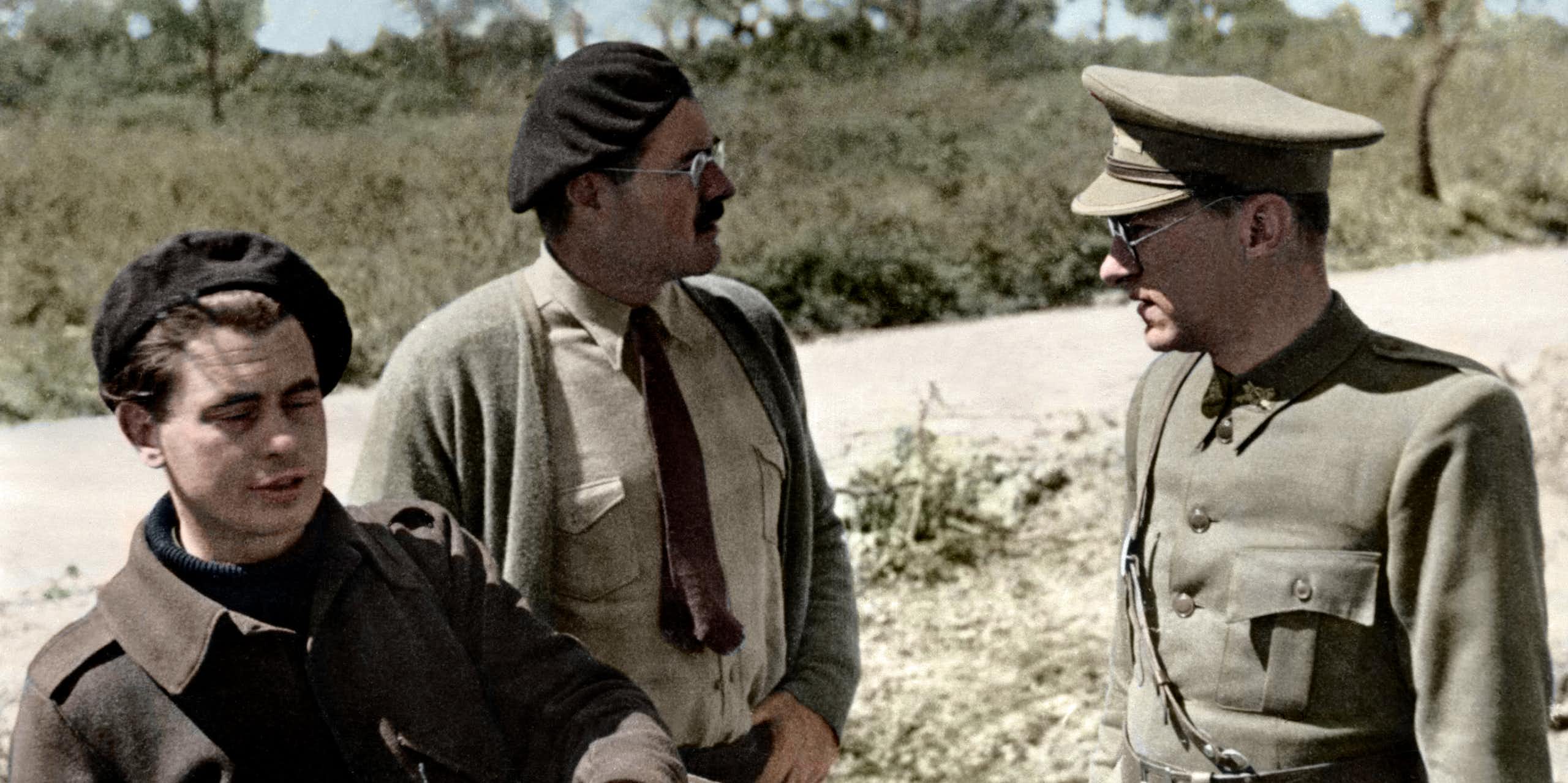 Dos hombres de paisano hablan con un hombre vestido de soldado en un campo.