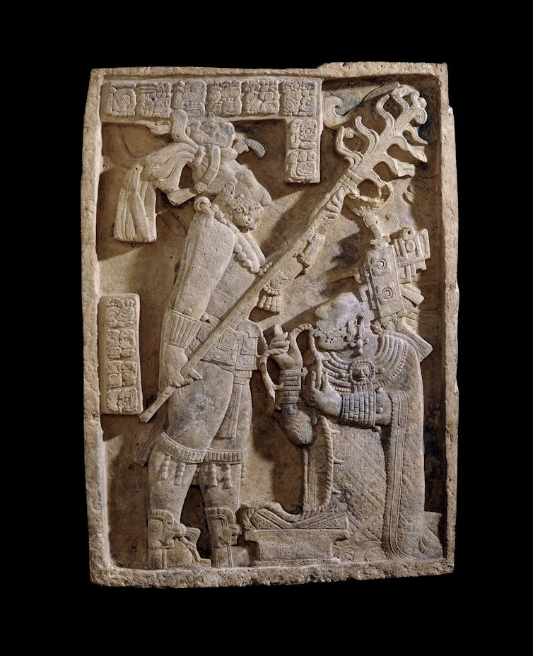 A carved limestone lintel depicting a bloodletting ritual in which a man holds a burning torch over a woman pulling a rope through her tongue.