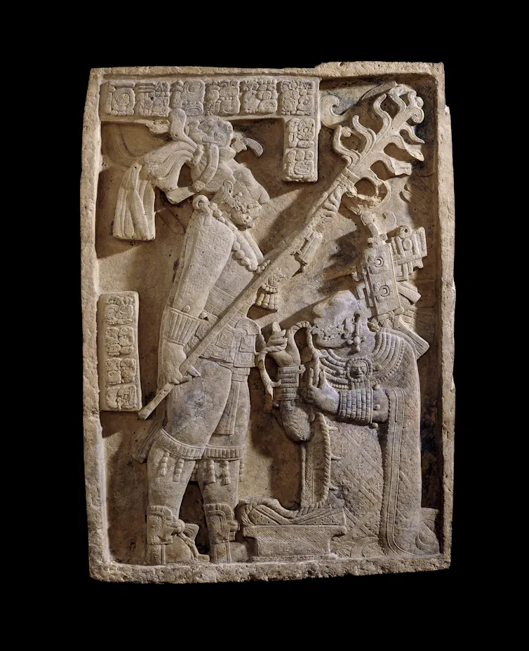 A carved limestone lintel, showing a bloodletting ritual, in which a man holds a flaming torch over a woman, who is pulling a rope through her tongue.