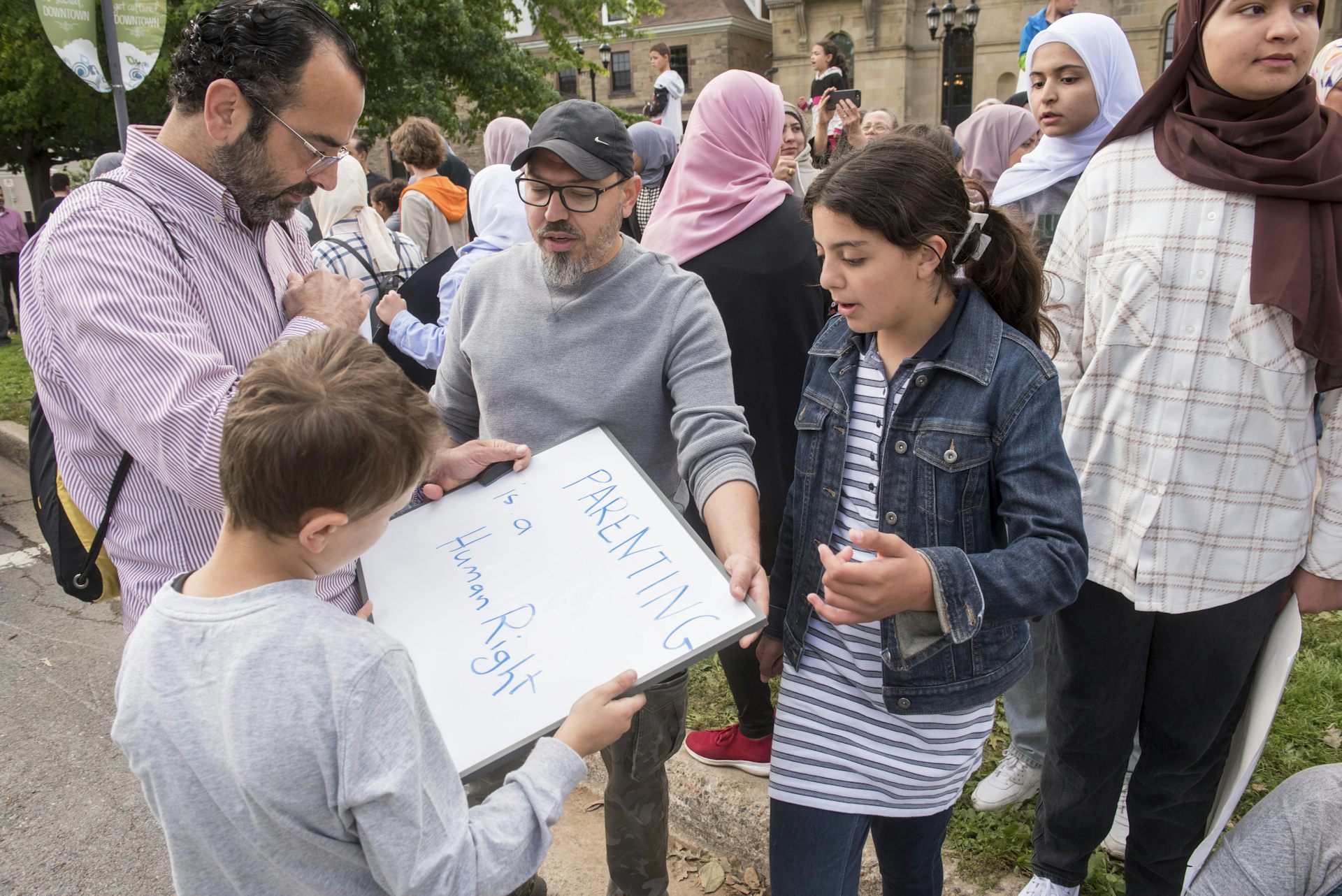 A man holds a sign that says parenting is a human right at a rally surrounded by people.
