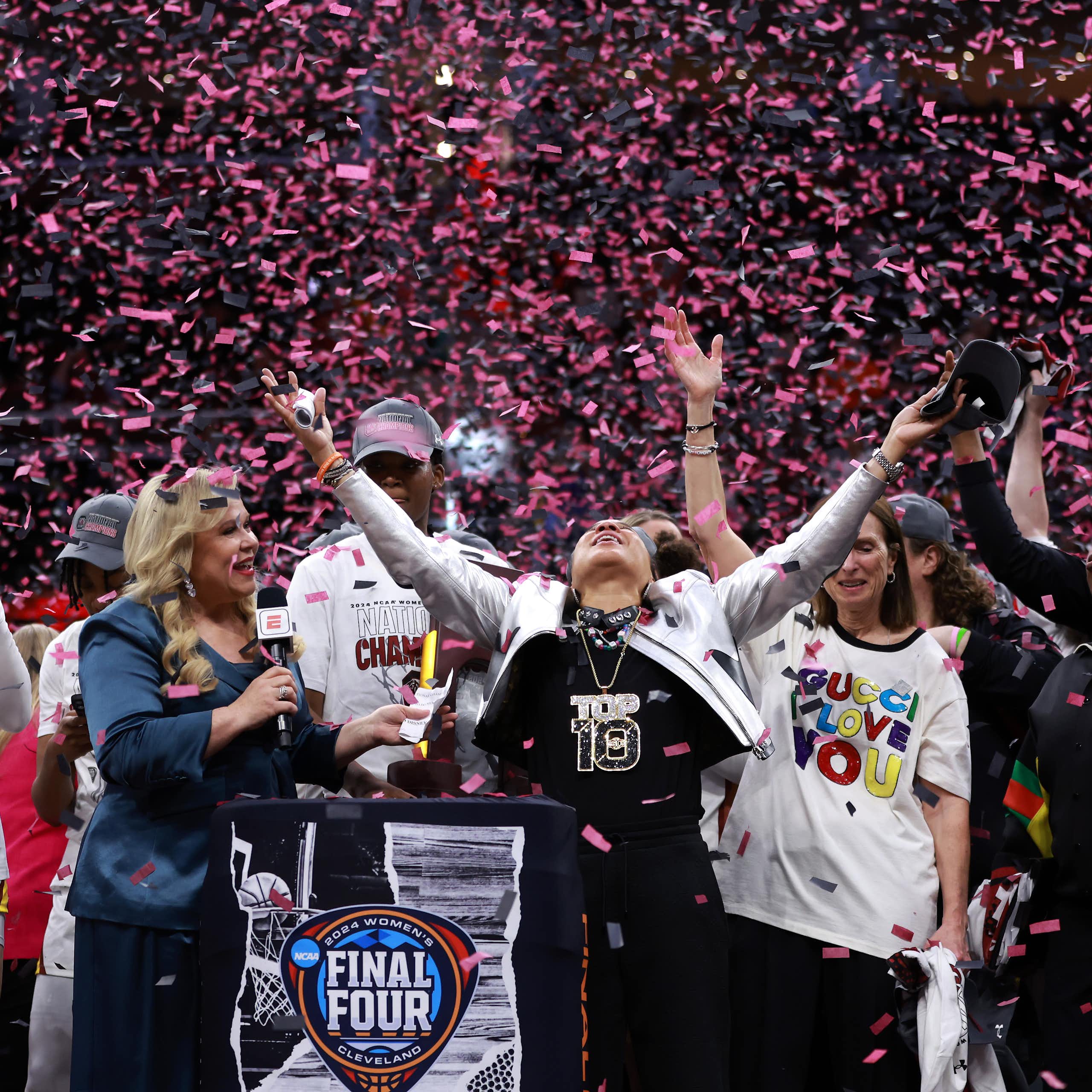 Pink confetti falls from the rafters of a basketball arena as a female coach and her players celebrate.