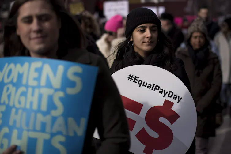 Two demonstrators holding signs, one sign says women's rights are human rights and one says equal pay day.