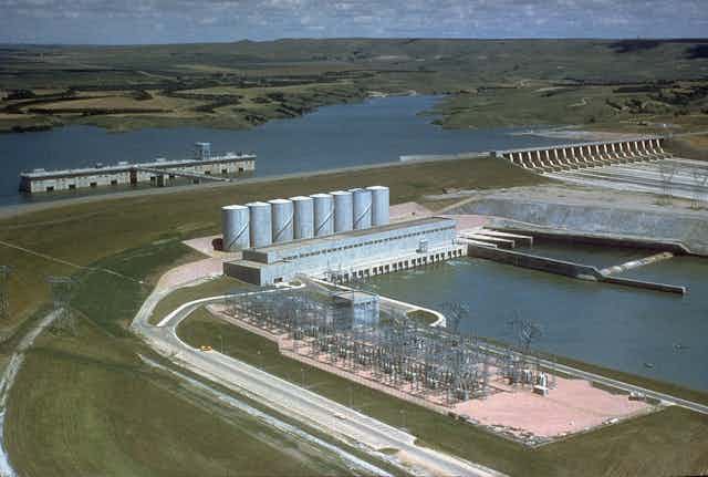A large dam with a spillway stretches in front of a reservoir