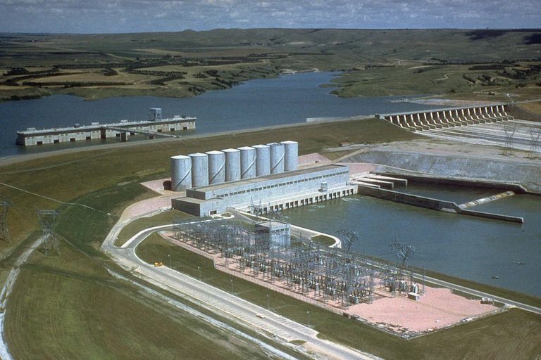 A large dam with a spillway stretches in front of a reservoir