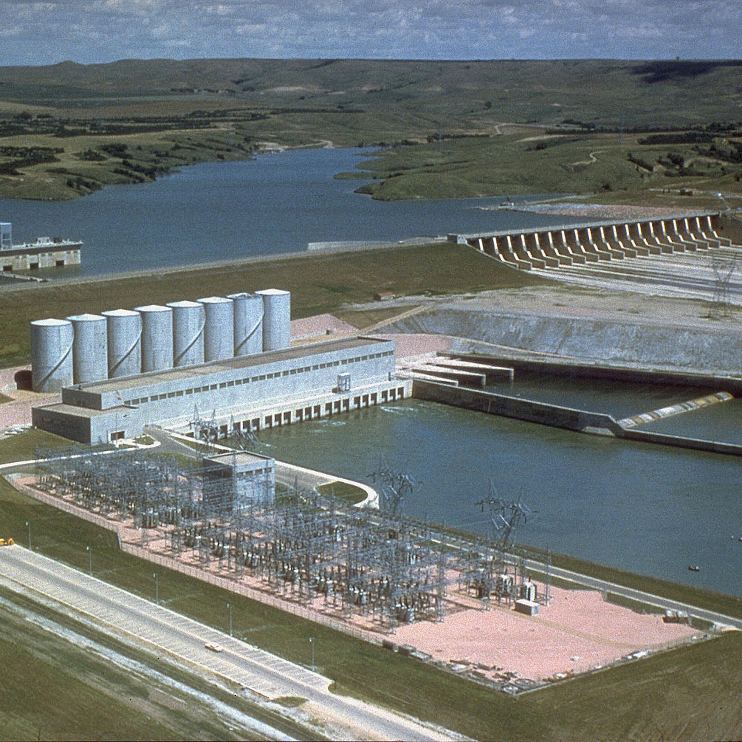 A large dam with a spillway stretches in front of a reservoir