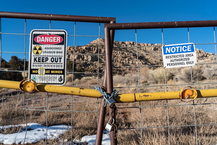 Signs on a wire fence read 'Danger,' 'Abandoned Uranium Mine' and 'Restricted Area'