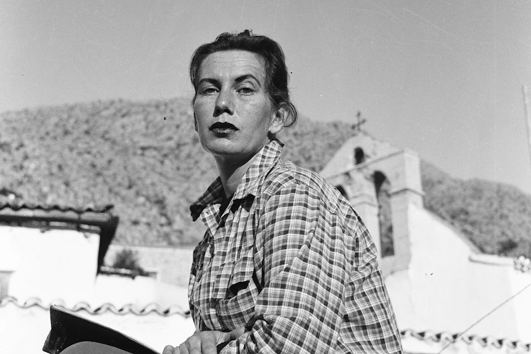Charmian Clift sits in front of a white church on the island of Hydra.