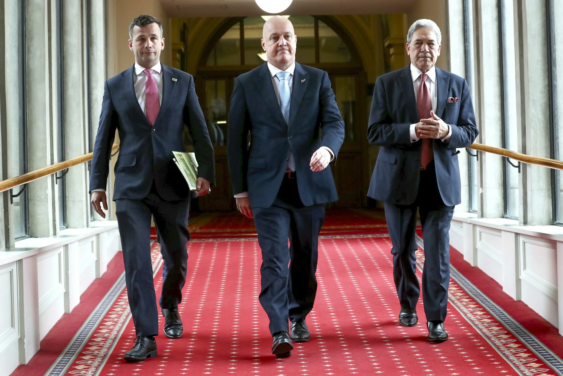 David Seymour, Christopher Luxon and Winston Peters walking toward camera in parliament corridor