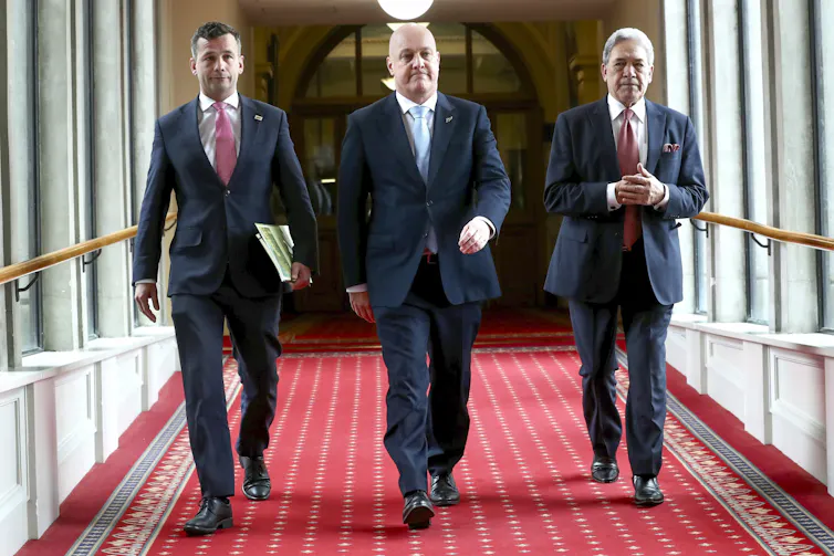 David Seymour, Christopher Luxon and Winston Peters walking toward camera in parliament corridor