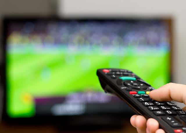 A person uses their remote control to watch sport on TV