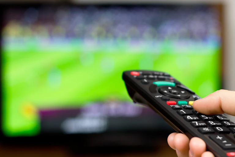 A person uses their remote control to watch sport on TV