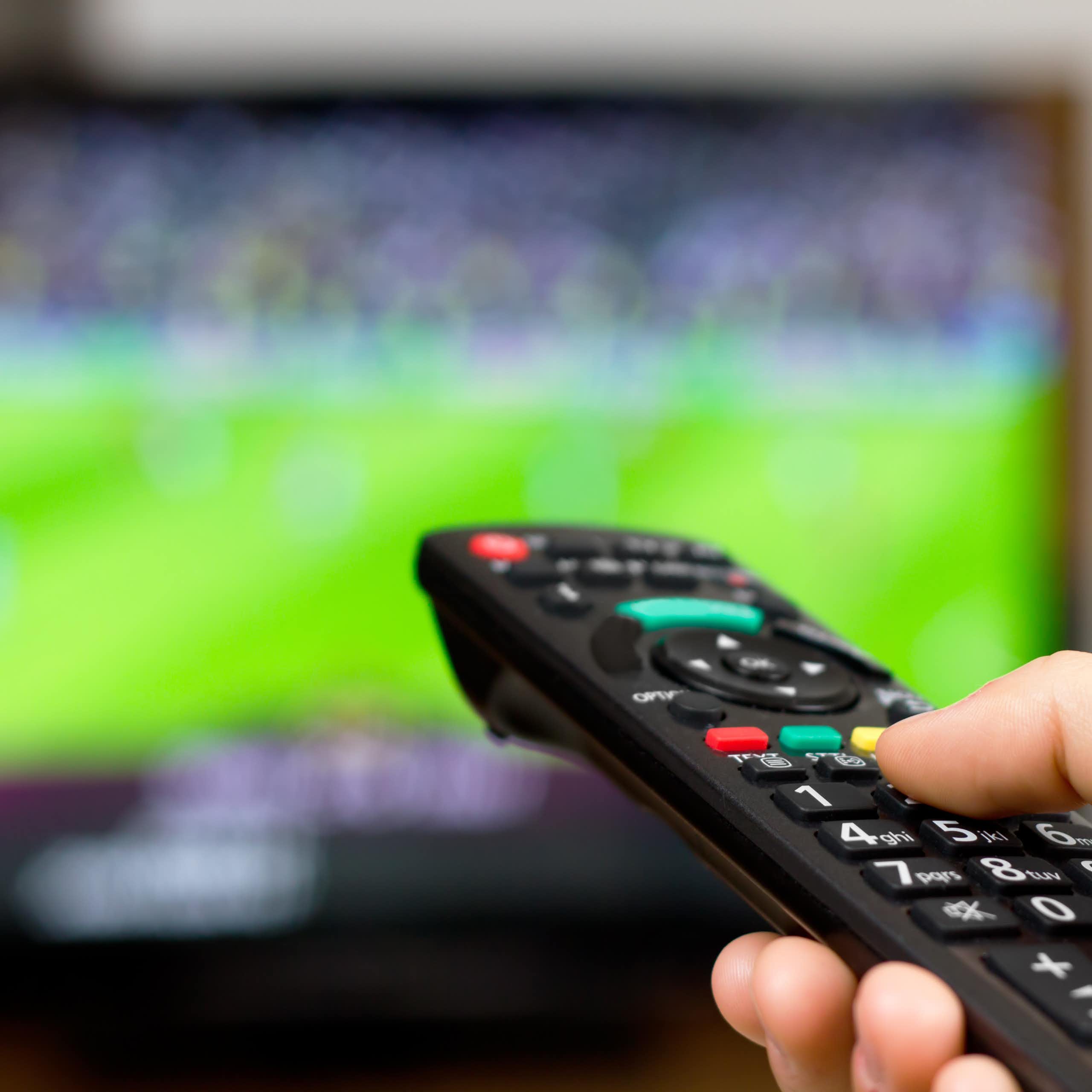 A person uses their remote control to watch sport on TV
