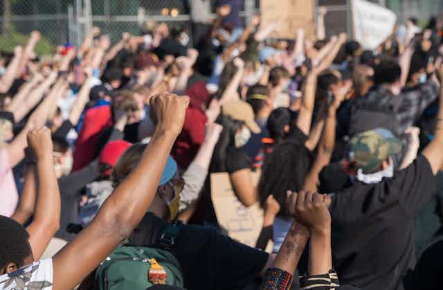 People at a protest raising their hands with their fists clenched. 