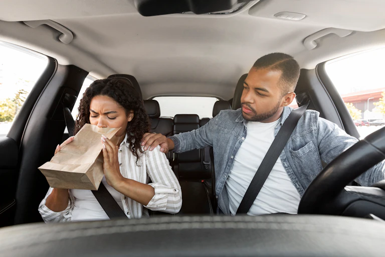 Passagère d'une voiture éprouvant un malaise et tenant un sac en papier pour vomir.