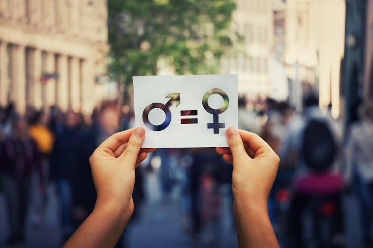 Woman's hands holding a white paper sheet with male and female symbol over a crowded city street background