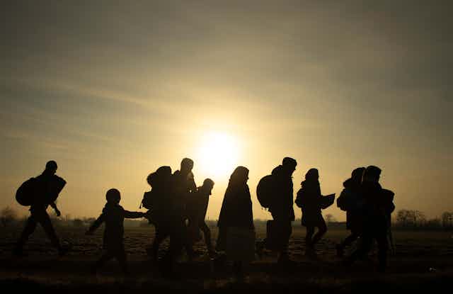 Side view of silhouettes of a group of people of different ages and genders walking across a field with the sun illuminating the background