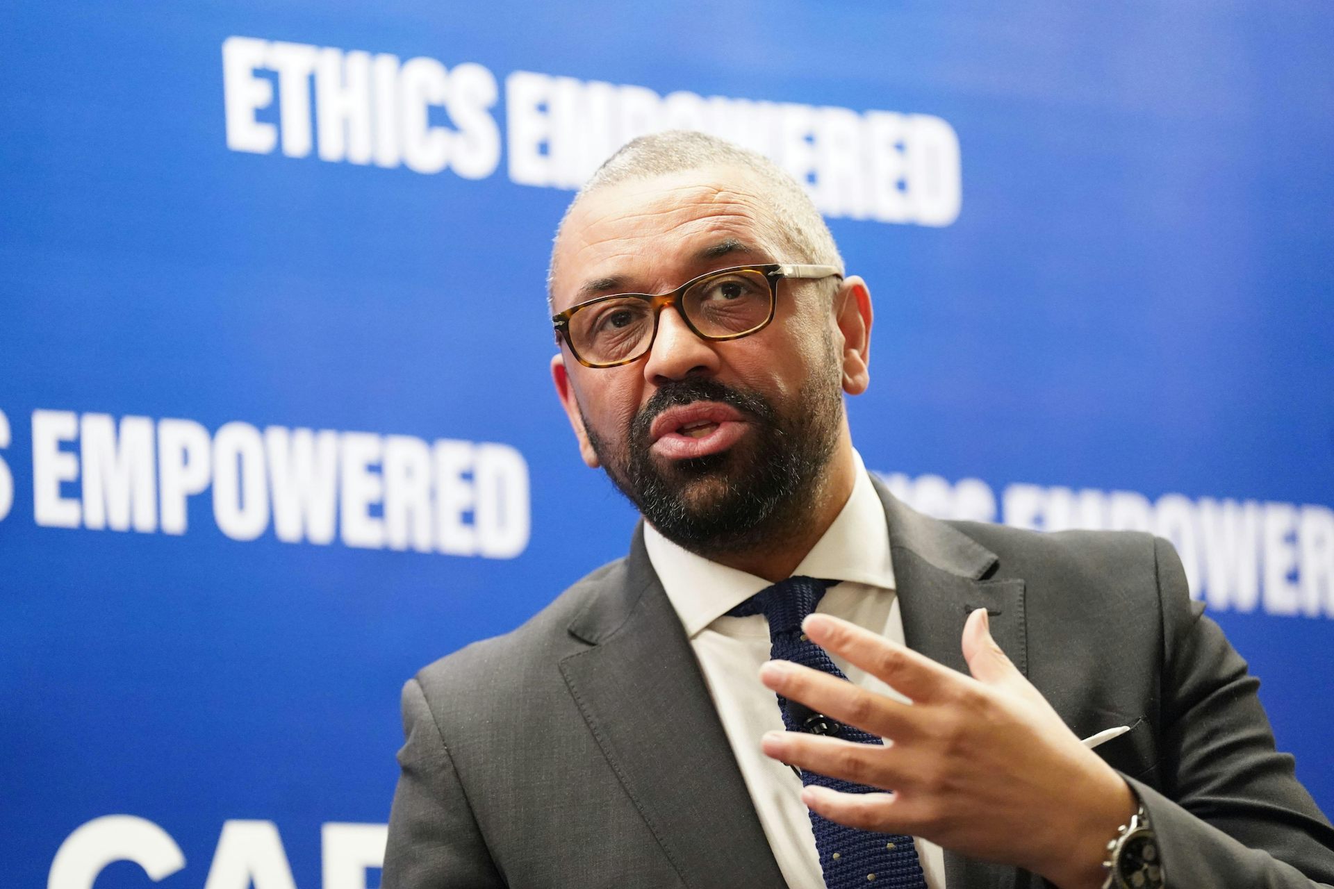 James Cleverly speaking in front of a blue wall reading 'ethics empowered'