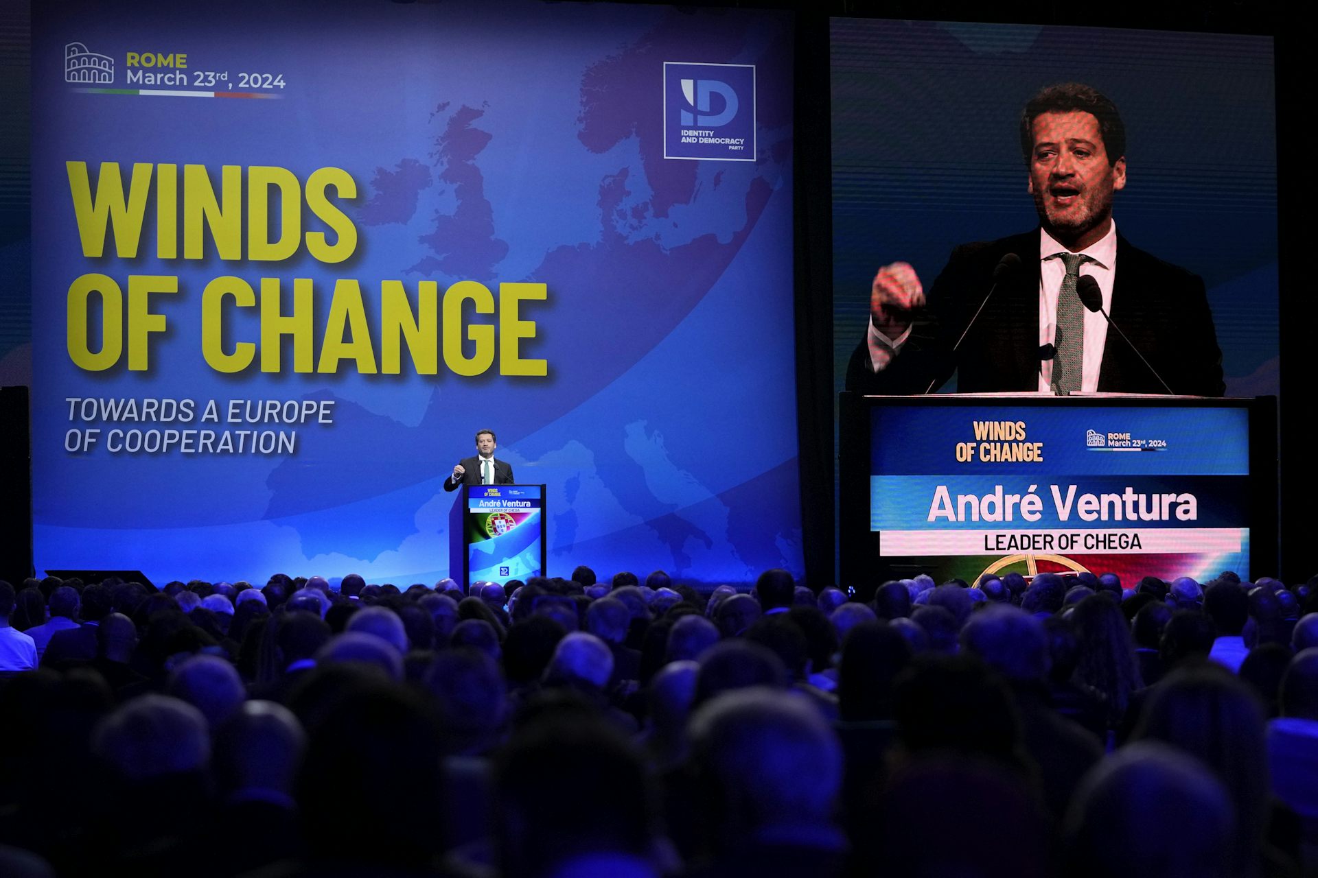 A man speaks at a podium with a Winds of Change sign behind him.