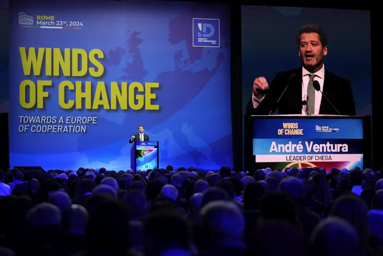 A man speaks at a podium with a Winds of Change sign behind him.