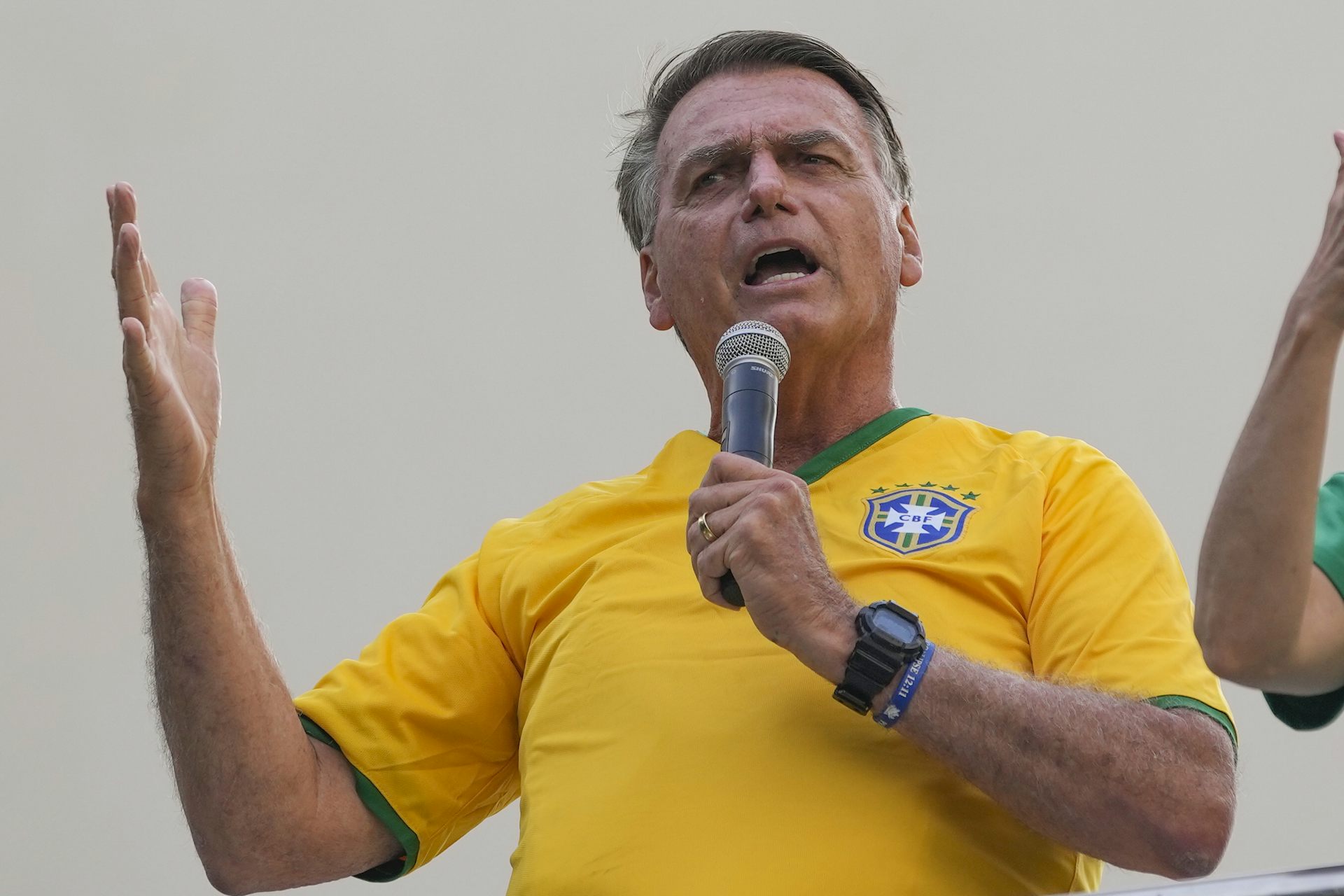 A man in a yellow shirt speaks into a microphone while gesturing.