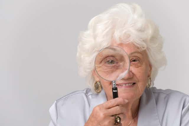 Woman with white hair holding a magnifying glass up to one eye